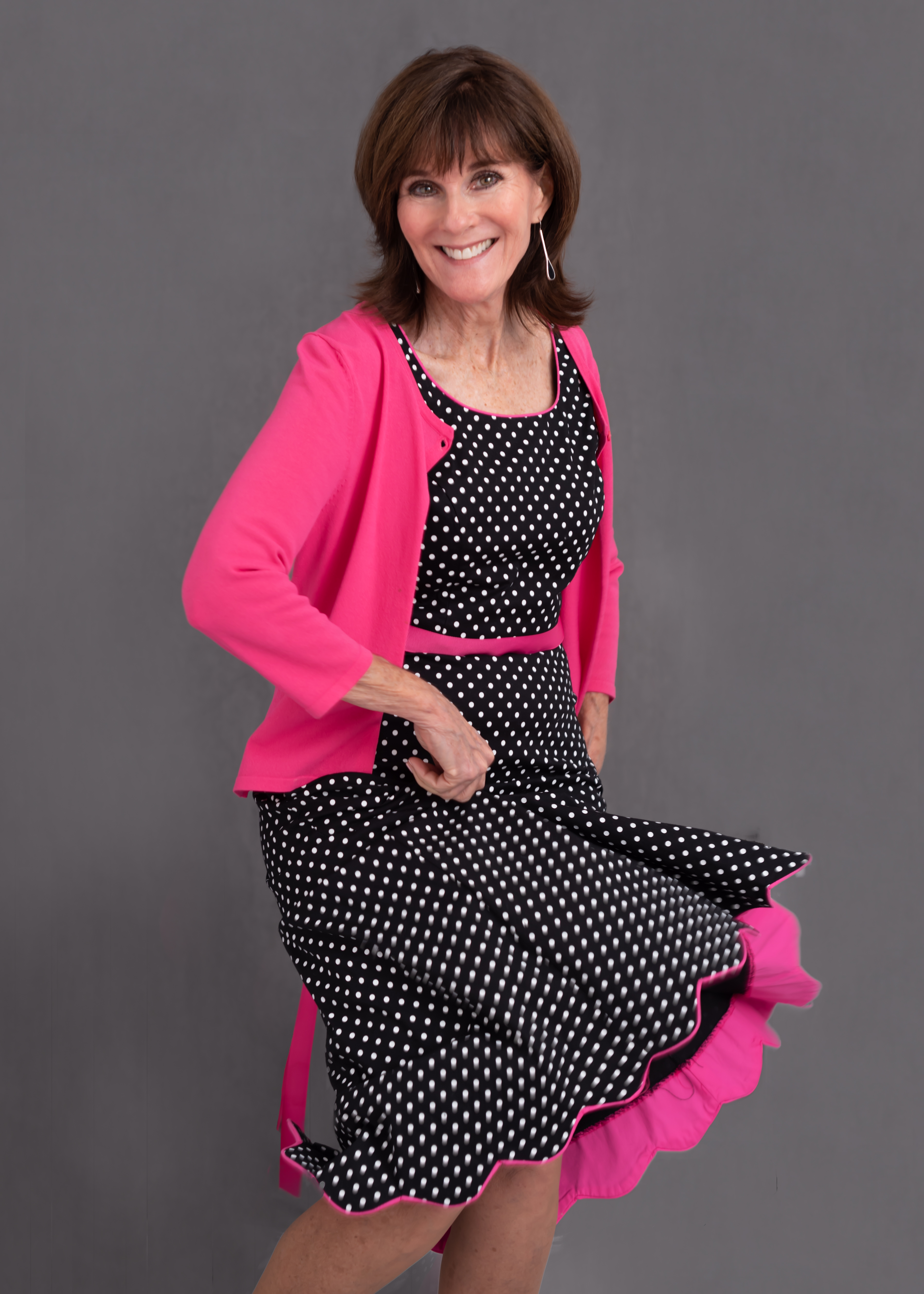 Coach Bernadette smiling in a black-and-white polka dot dress with a pink cardigan.